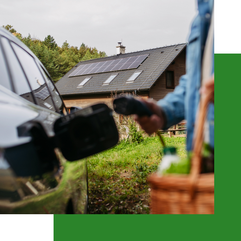 Ein schwarzes Elektroauto steht mit geöffneter Ladebuchse vor einem modernen Einfamilienhaus mit Solarpanelen auf dem Dach. Im Vordergrund hält eine Person in einer Jeansjacke ein Ladekabel in der Hand, bereit, das Auto aufzuladen. In der anderen Hand trägt sie einen Einkaufskorb mit Getränken. Die Szene vermittelt den nachhaltigen Ansatz, ein Elektroauto mit selbst erzeugtem Solarstrom zu laden.