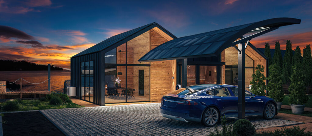 Ein modernes Holzhaus mit großen Glasfronten steht idyllisch am Wasser in der Abenddämmerung. Im Vordergrund lädt ein blaues Elektroauto unter einem überdachten Carport mit Solardach. Die stilvolle Außenbeleuchtung betont die nachhaltige Architektur des Hauses, während drinnen ein gemütlicher Essbereich sichtbar ist.