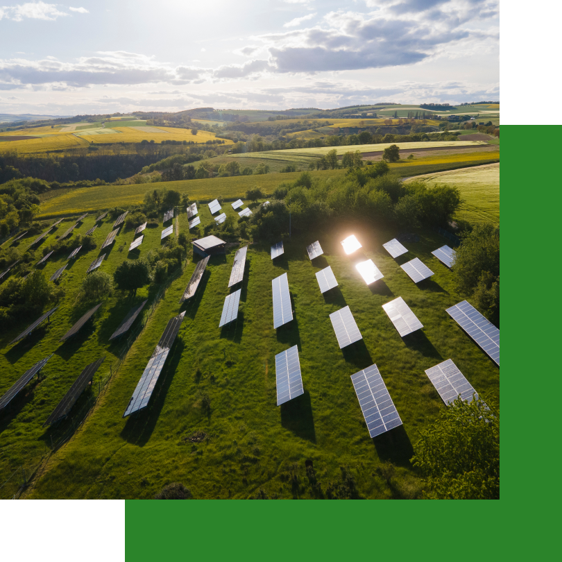 Ein großer Solarpark inmitten einer hügeligen Landschaft mit grünen Wiesen und Feldern. Zahlreiche Solarpaneele sind in Reihen aufgestellt und reflektieren das Sonnenlicht. Der Himmel ist teils bewölkt, doch die Sonne scheint und sorgt für nachhaltige Energiegewinnung.