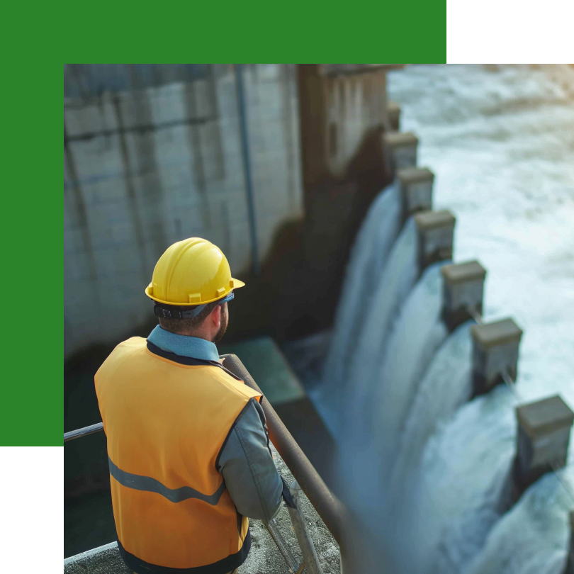 Ein Arbeiter in einer gelben Sicherheitsweste und einem Schutzhelm steht auf einer Plattform und blickt auf ein großes Wasserkraftwerk. Mehrere Schleusen lassen mit hoher Geschwindigkeit Wasser durch, das zur Energieerzeugung genutzt wird. Die Szene ist von natürlichem Licht beleuchtet, das die nachhaltige Energiegewinnung unterstreicht.